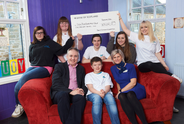 People sitting on sofa with an oversized check held overhead