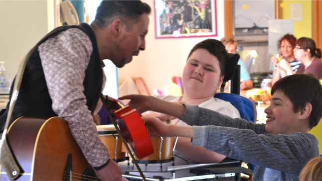 Man with Guitar in class room playing to two children