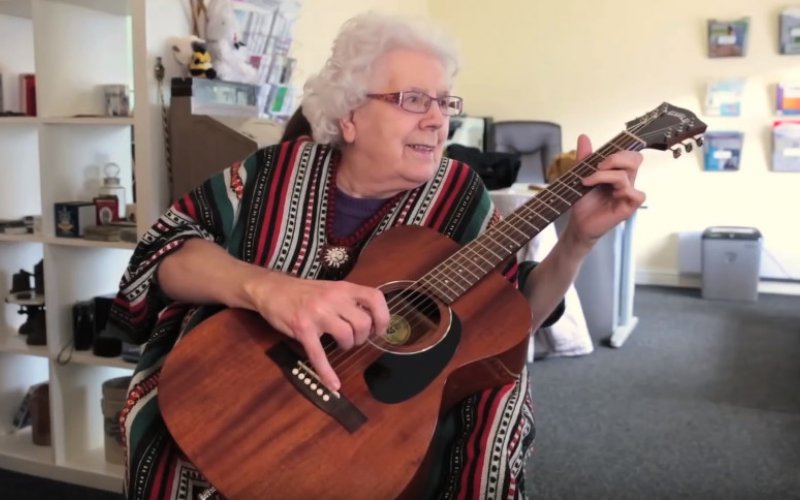 Grey haired woman playing a guitar